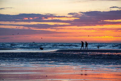 Silhouette people on beach against sky during sunset