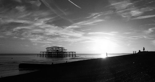 Silhouette pier on beach against sky
