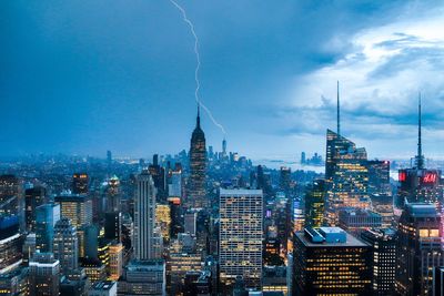 Illuminated buildings in city against cloudy sky