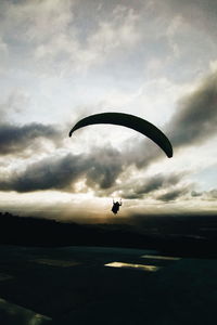 Person paragliding over sea against sky