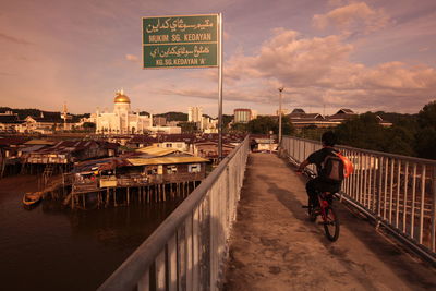 Boy riding cycling on bridge over river in town