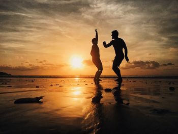 Silhouette friends dancing at beach against sky during sunset