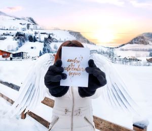 Close-up of woman holding text on paper against sky during winter