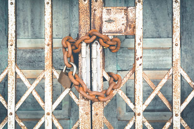 Close-up of padlock and rusty chain wrapped on metallic gate