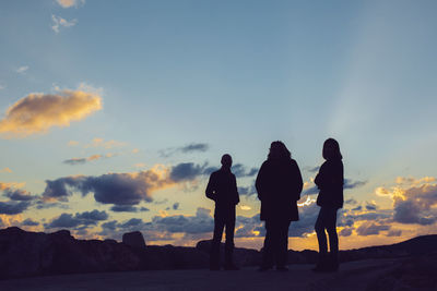 Silhouette people standing on land against sky during sunset