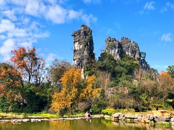 Trees by rocks against sky during autumn