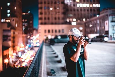 Woman photographing illuminated city street at night