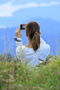 Rear view of woman photographing on mobile phone against sky