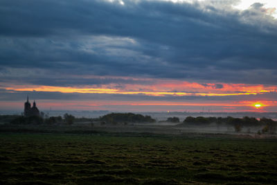 Scenic view of field against dramatic sky during sunset