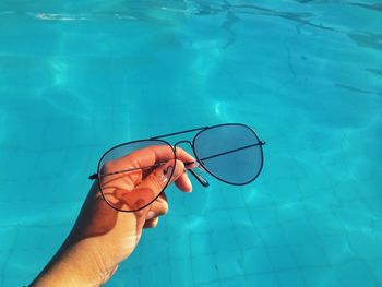 Close-up of person holding sunglasses against swimming pool