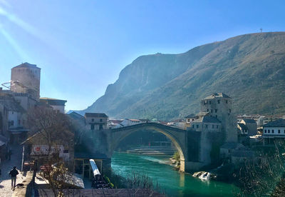 Bridge over river amidst buildings in city against sky