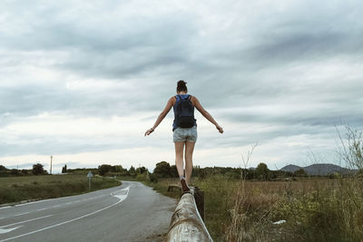 Rear view of man standing on road against cloudy sky