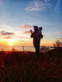 Women and her son standing on field against sky during sunset