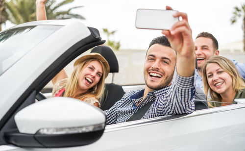 Happy friends taking selfie while traveling in convertible