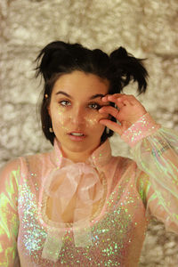 Portrait of young woman standing against wall hand on face with glitter as well 