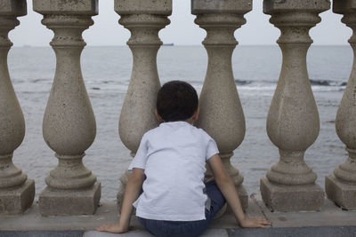 Rear view of boy sitting by balustrade