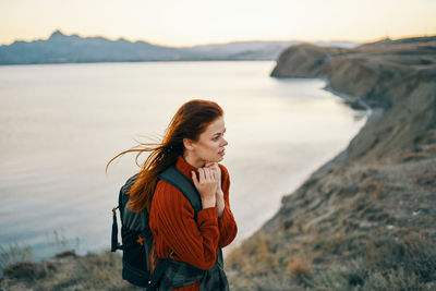 Young woman standing at shore against sky