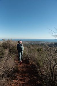 Rear view of woman walking on field against clear sky