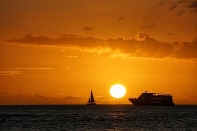 Silhouette sailboat in sea against orange sky