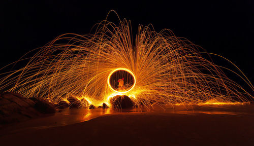 Light trails on illuminated land against sky at night