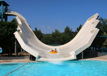 People swimming in pool against blue sky