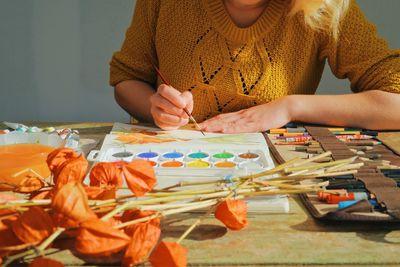 Midsection of woman painting in paper at table