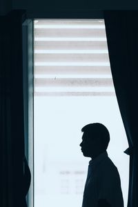 Silhouette man looking through window