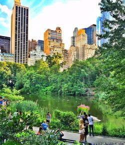 People by river in city against sky