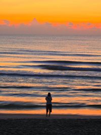 Silhouette man standing on beach against orange sky