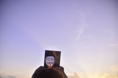 Low angle view of man wearing mask looking in mirror against sky during sunset