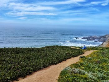 Man looking at sea against sky while sitting on mountain