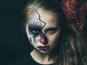 Close-up portrait of woman with painted face against black background