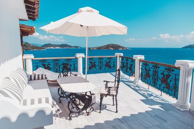 Chairs and table by swimming pool against sea