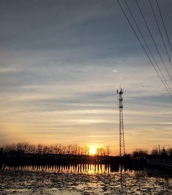 Silhouette trees and electricity pylon against sky during sunset