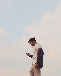 Side view of man using mobile phone against sky while music on