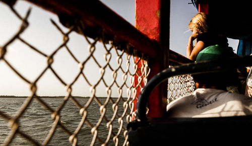 Rear view of woman looking through chainlink fence