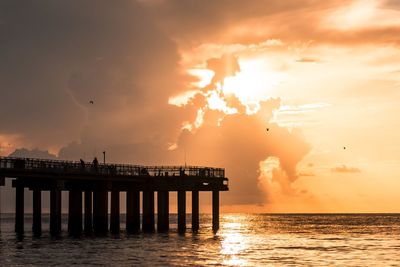 Silhouette pier over sea against sky during sunset