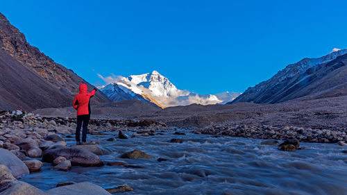 Rear view of woman standing on rock by flowing stream against clear sky