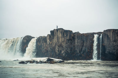 Mid distance of man standing at waterfall against clear sky