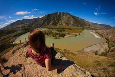 Rear view of woman sitting on mountain against sky