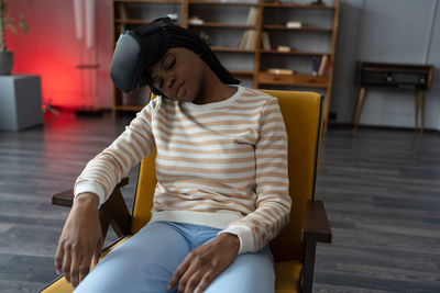 Black young woman removed virtual reality goggles and fell asleep after watching series in armchair.