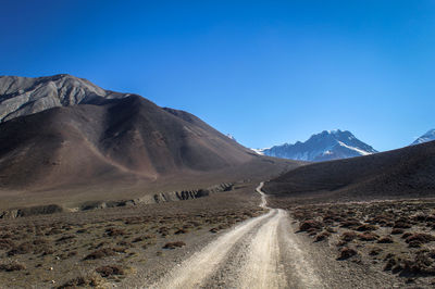 Road leading towards mountains against blue sky