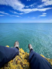 Low section of man sitting on beach against sky