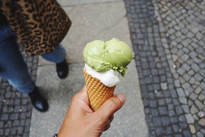 Cropped hand holding ice cream cone by woman standing on footpath