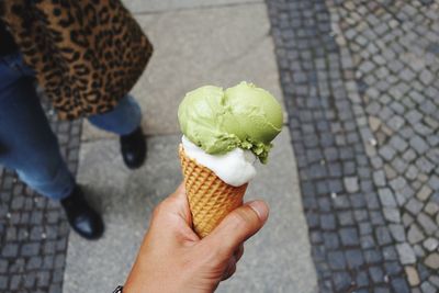 Low section of woman holding ice cream cone on footpath