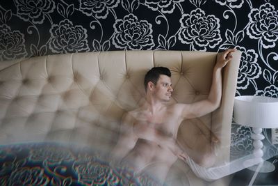 Double exposure of shirtless man against headboard
