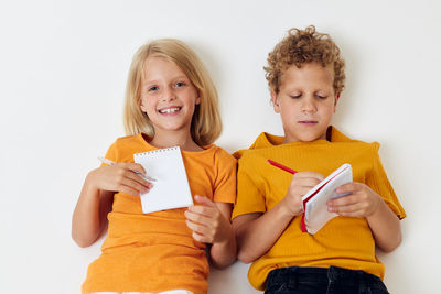 Cute sibling writing on textbook against white background