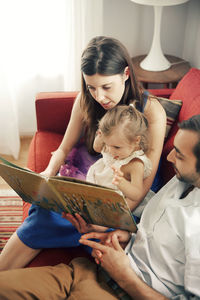 Man and woman showing picture book to girl while sitting on sofa at home