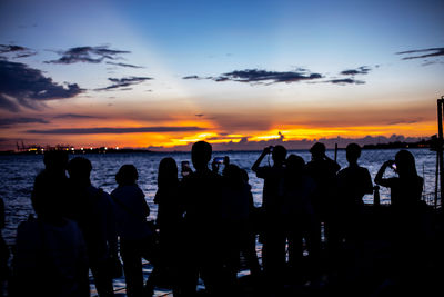 Silhouette people on beach against sky during sunset