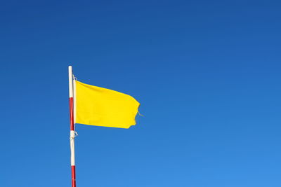 Low angle view of flag against clear blue sky